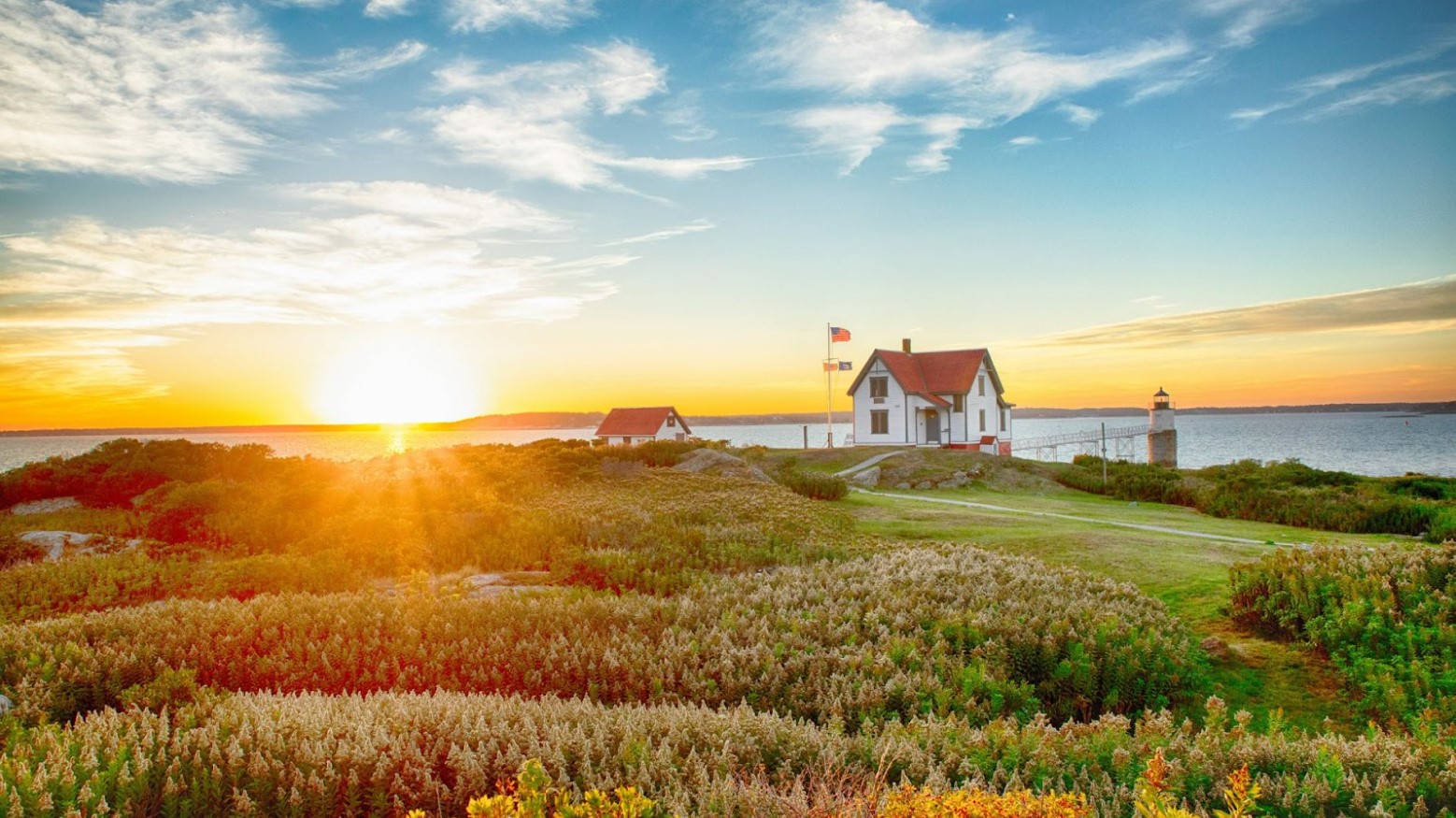 Small white homes seen near green pastures in front of the ocean in Maine.