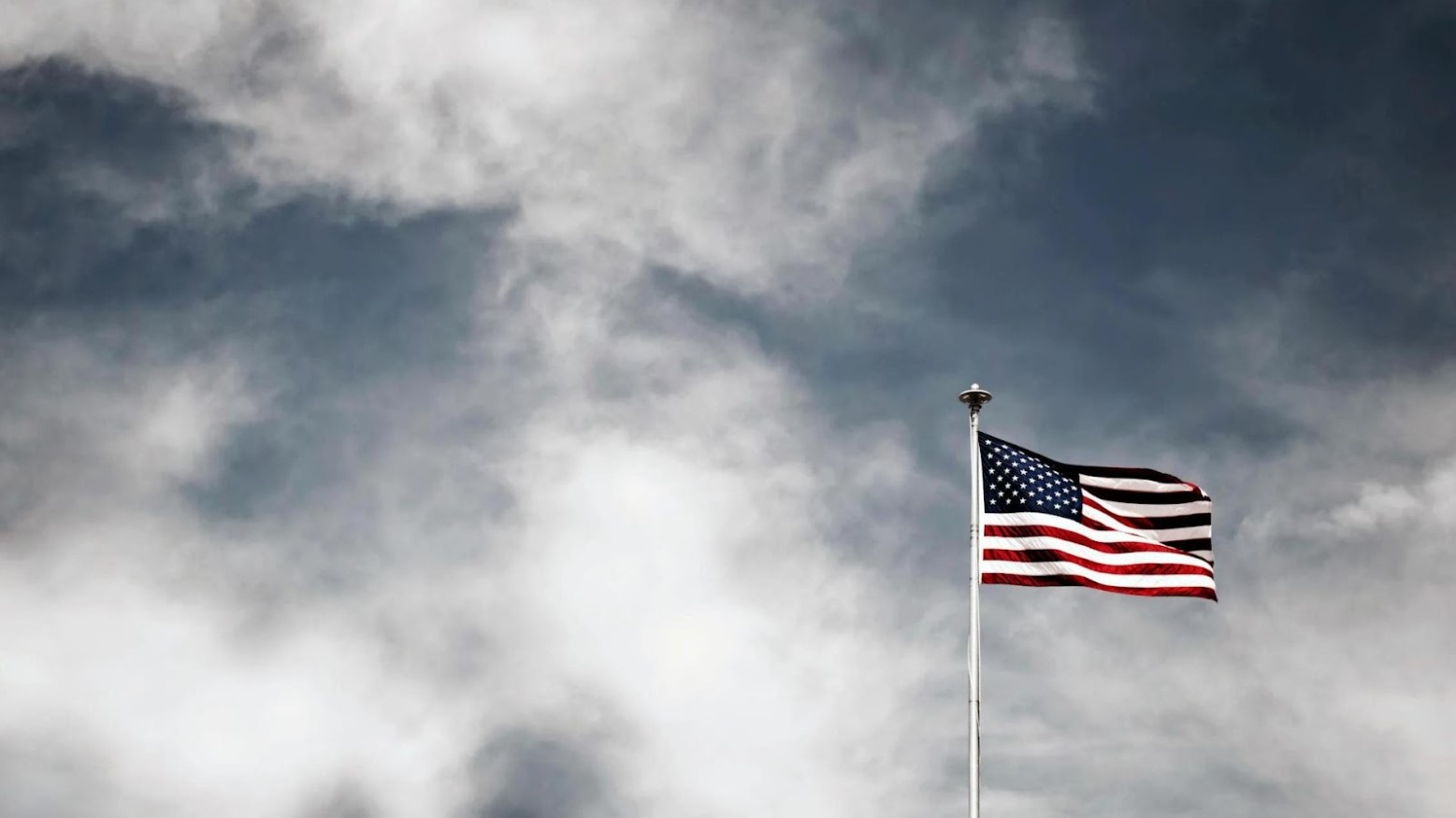 A US flag on a flagpole. The sky is grey and cloudy.