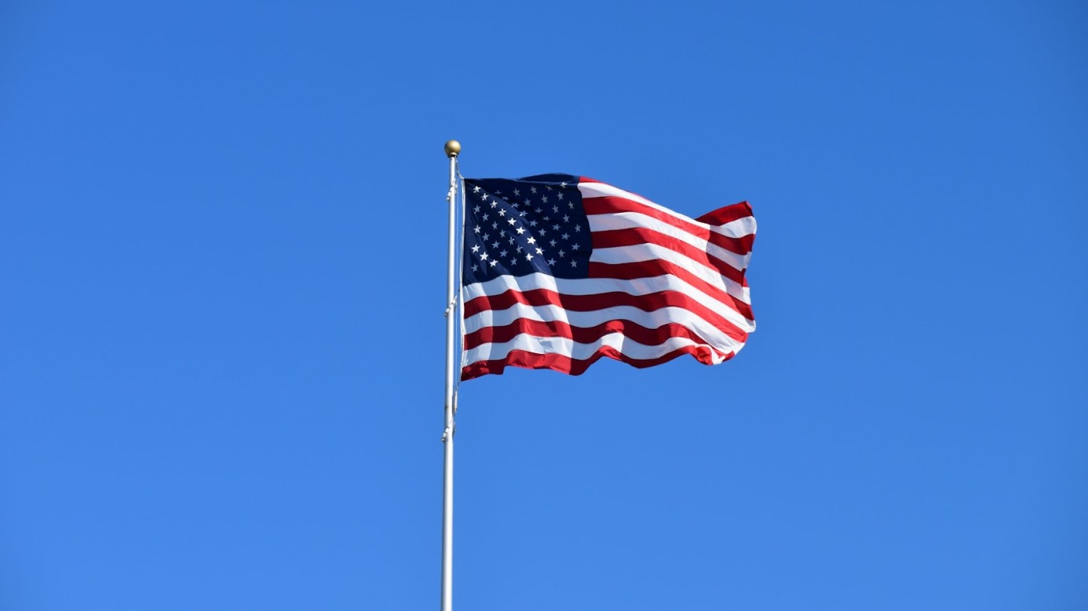 The American flag on a pole seen underneath a clear blue sky.