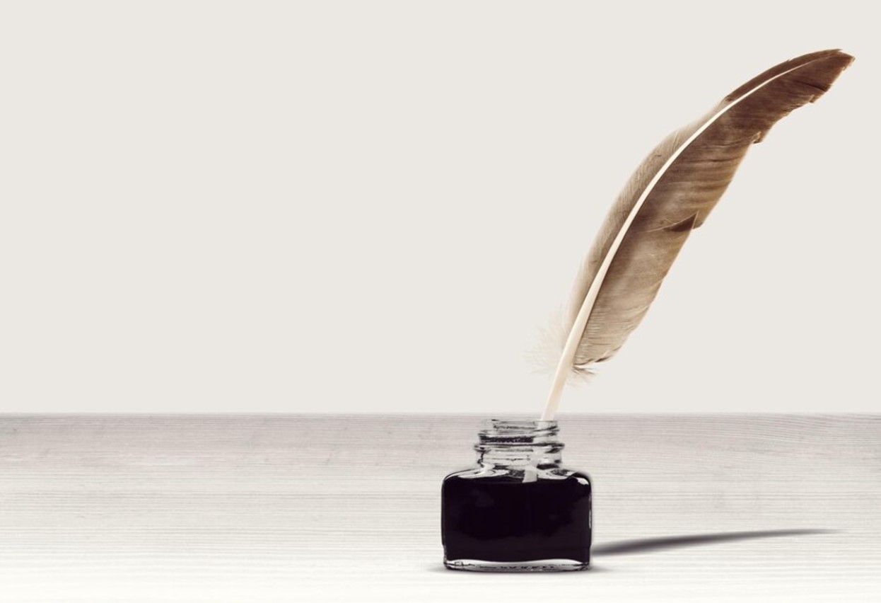 Photograph of a feather quill in a pot of ink against a white background