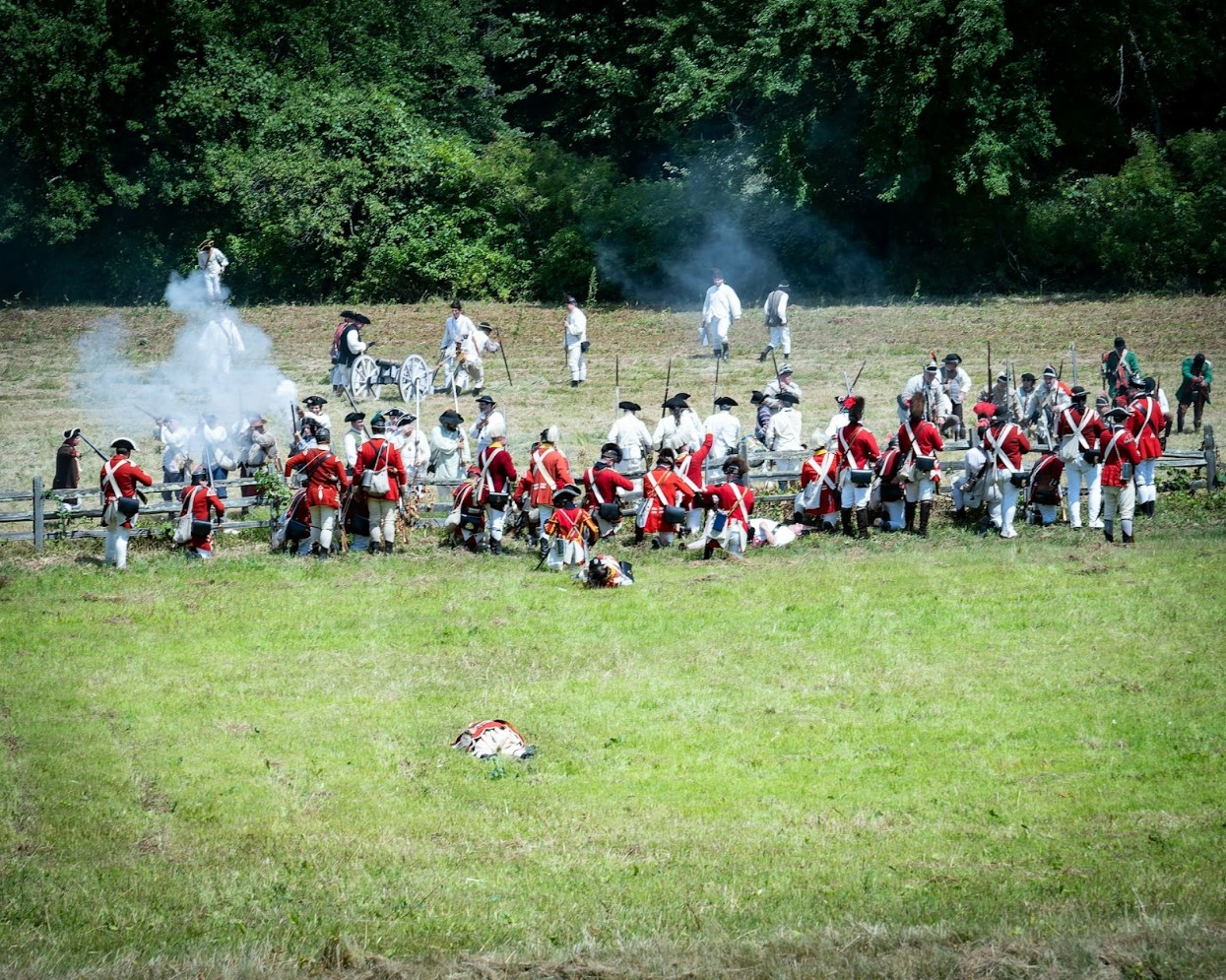 A group of people wearing red and white uniforms standing in a field reenacting a battle scene