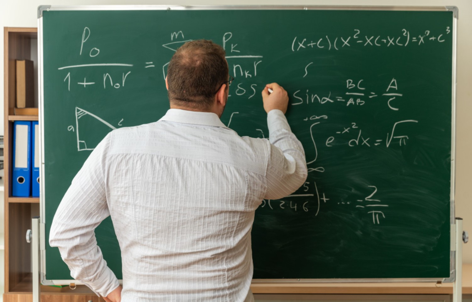 An image of a man writing on a large blackboard
