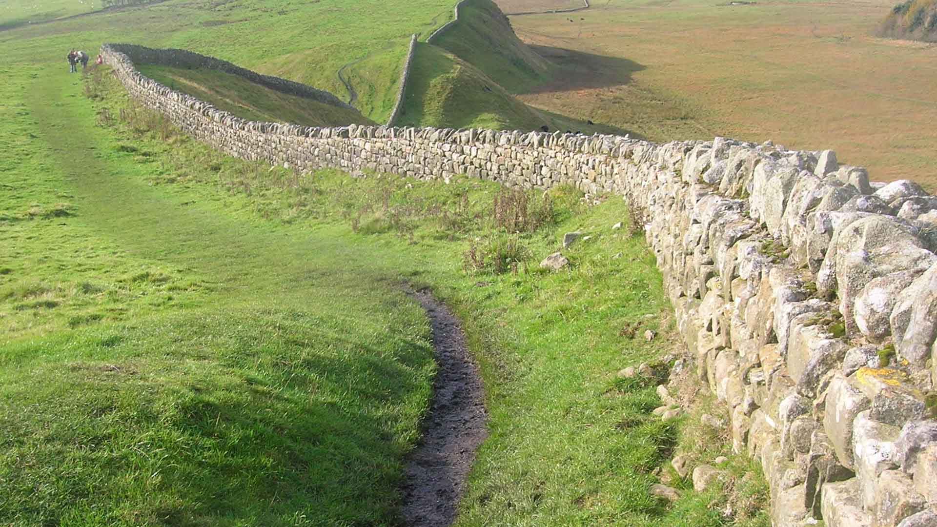 A view of Hadrian's Wall showing its length and height. The upright stones on top of it are modern, to deter people from walking on it.