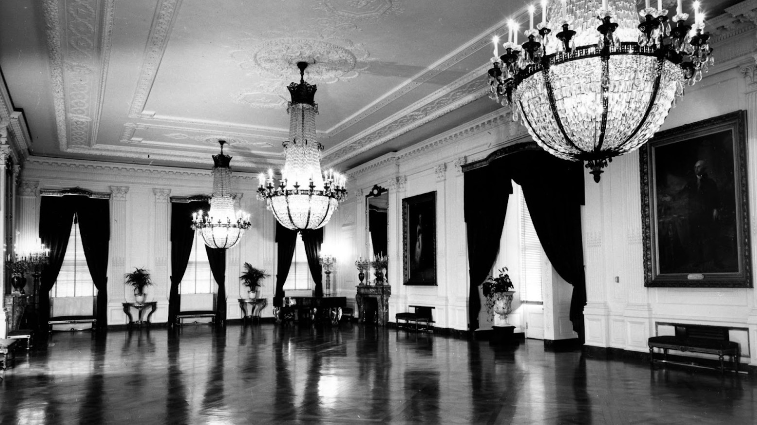 A 1947 black and white photo of the East Room in the White House which holds George and Martha Washington portraits.