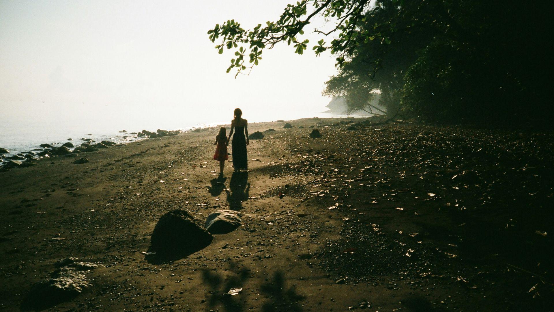 A mother and daughter holding hands and walking together outside.
