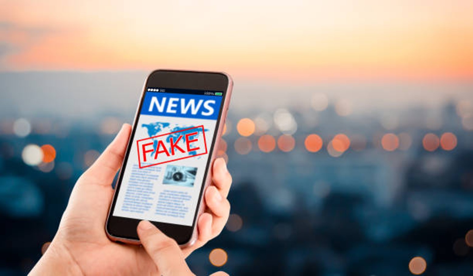A hand holds a phone open to the news with a red stamp that reads “Fake”