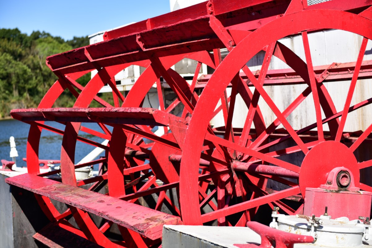 A large red paddle wheel is pictured at the rear end of a boat