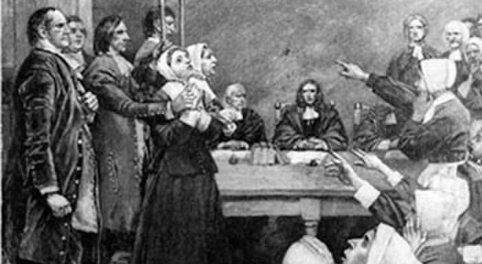 A black and white drawing of the Salem witch trials. Two ‘witches’ are on trial, and guards hold onto them. Some people sit at a desk, and others stand up and point at the ‘witches.’