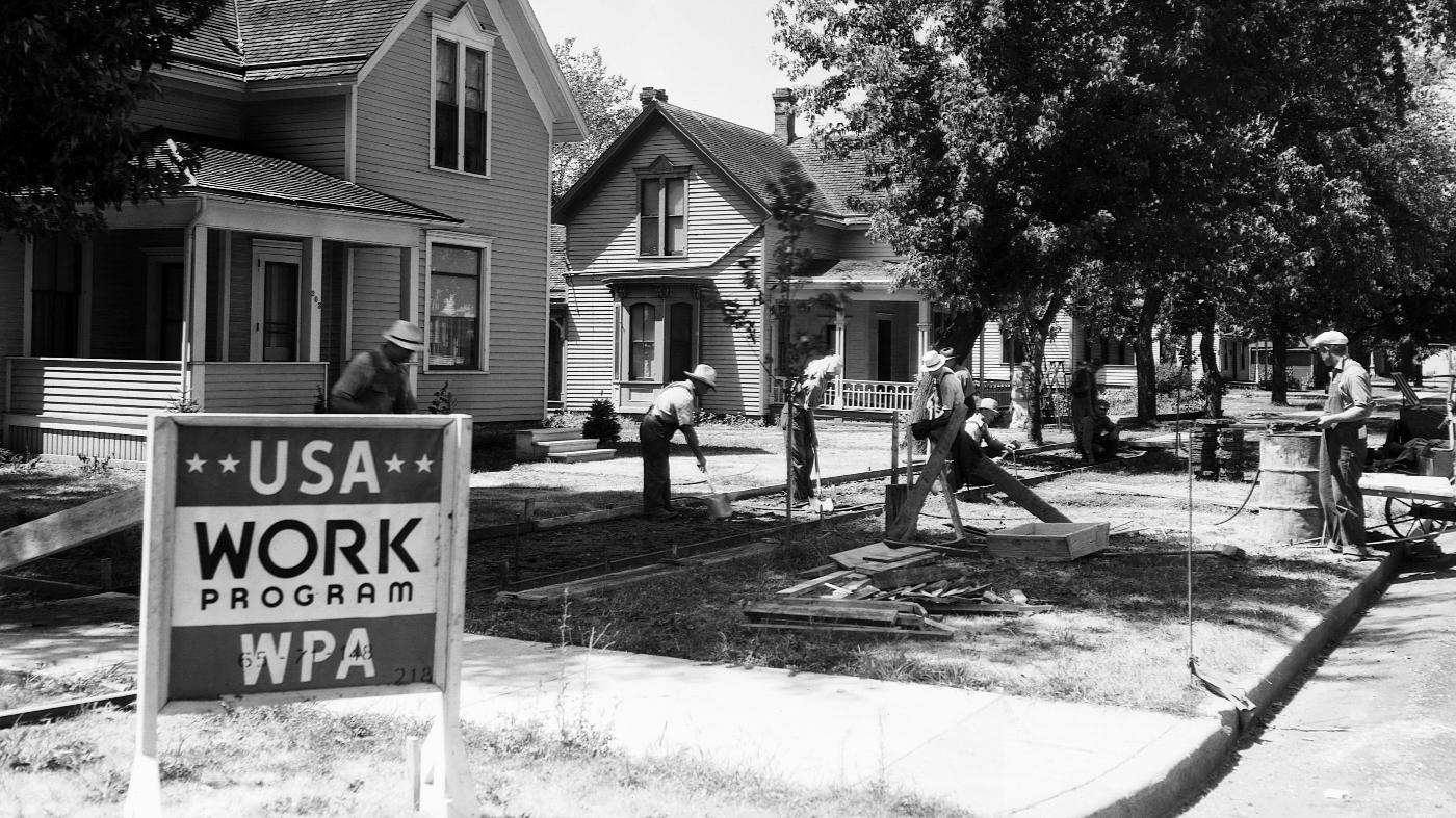 Several men work on neighborhood homes behind a sign that reads “USA Work Program WPA”