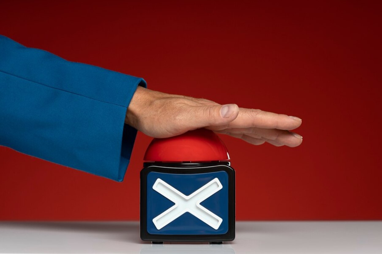 A man’s hand hits a red button with a blue and white “X” underneath it