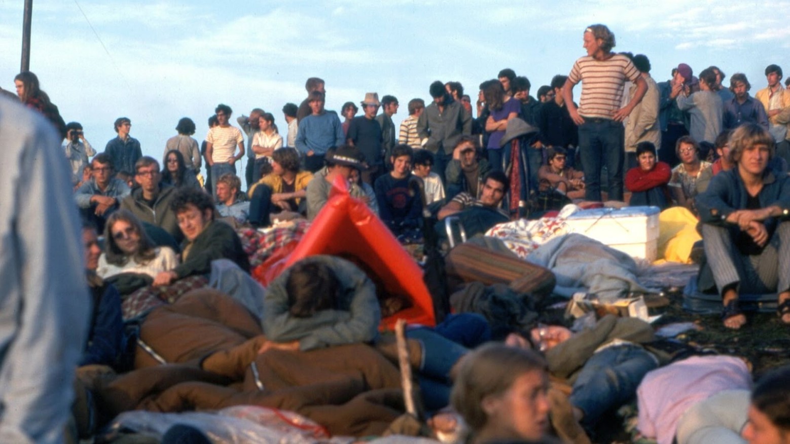 Many people waking up at Woodstock in 1969 and watching a performance.