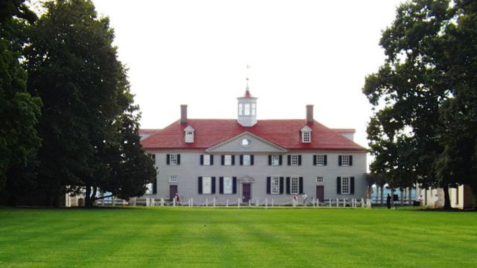 George Washington’s mansion. The house is white with a red roof and is surrounded by green grass and trees.