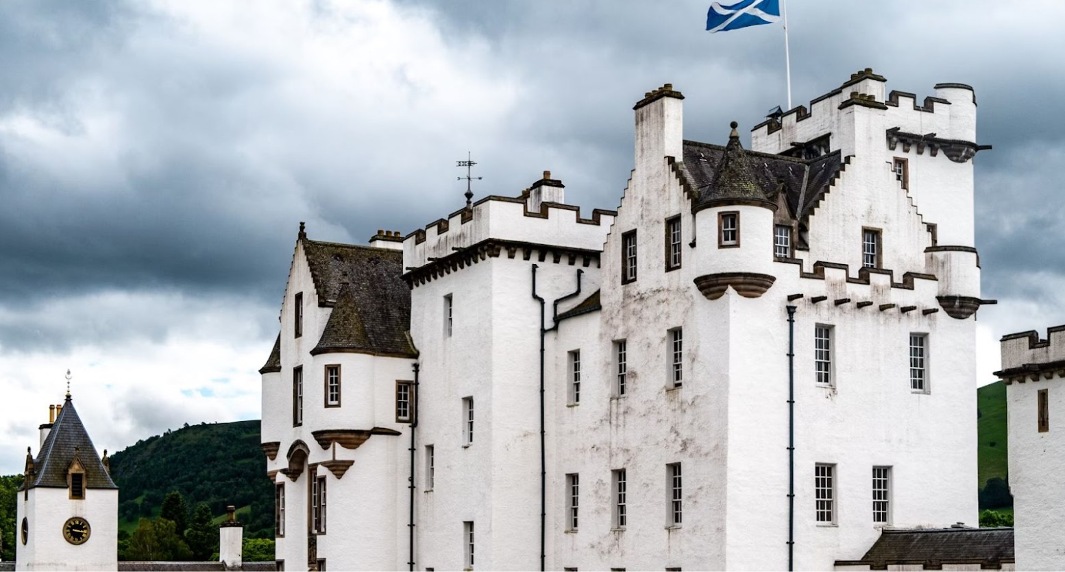 A white Scottish castle. At the top of the castle is a white flagpole with the Scottish flag on it.