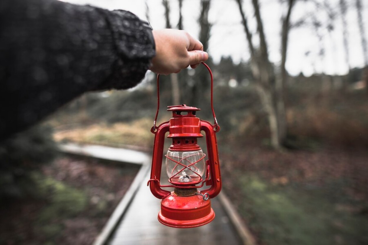 An outreached hand holds a kerosene lamp on a walk in the woods