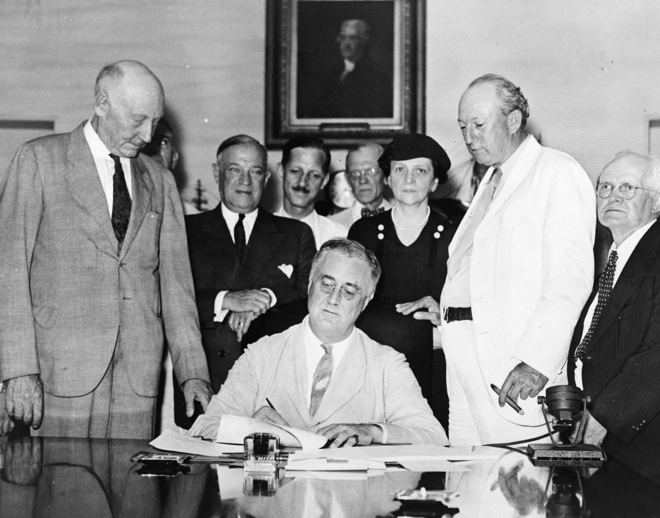 American President Franklin D. Roosevelt signed important legislation while his cabinet looked over his shoulder