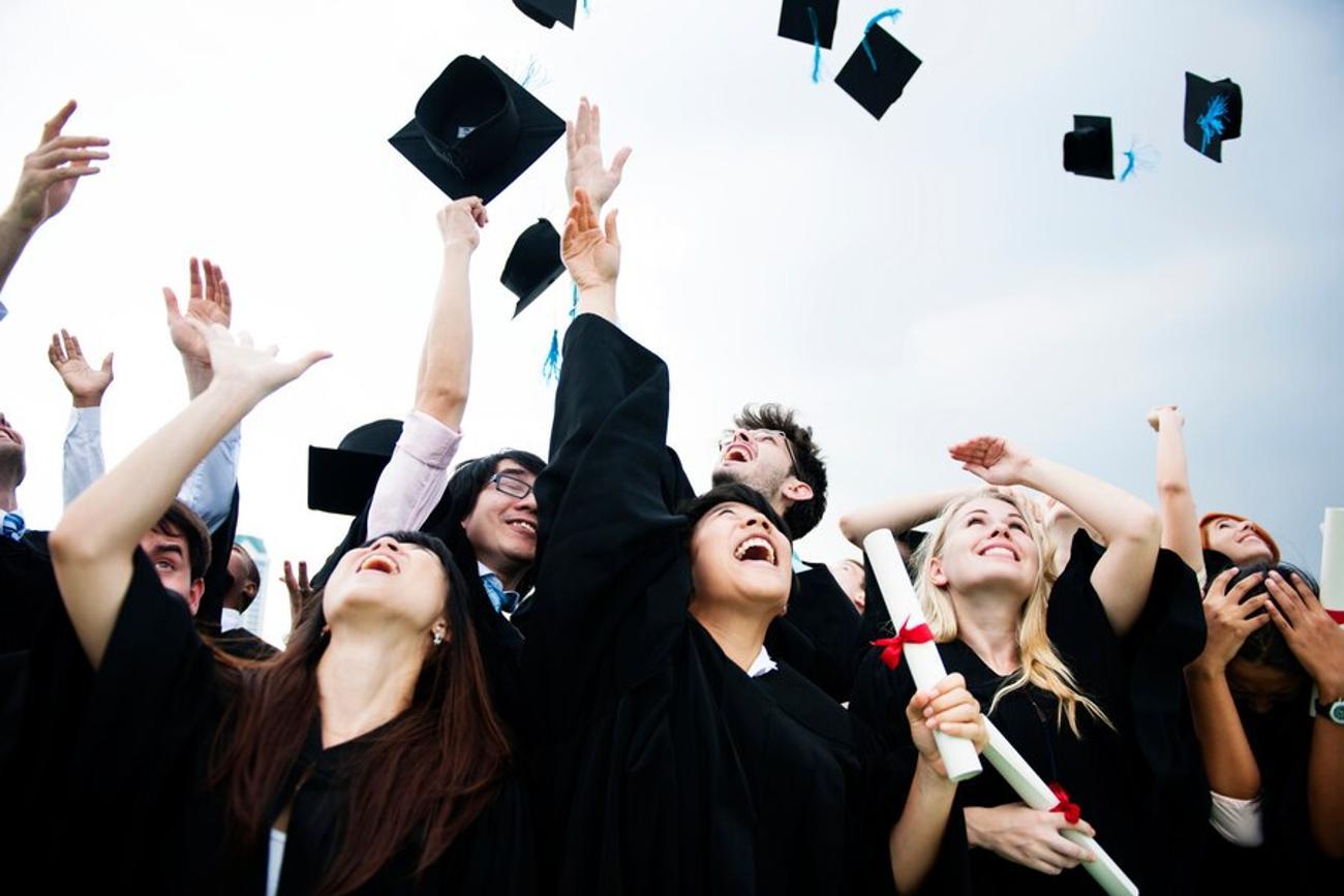 A class of college graduates throw their caps in the air at graduation