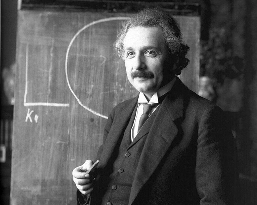 A black and white photograph of Albert Einstein in his office