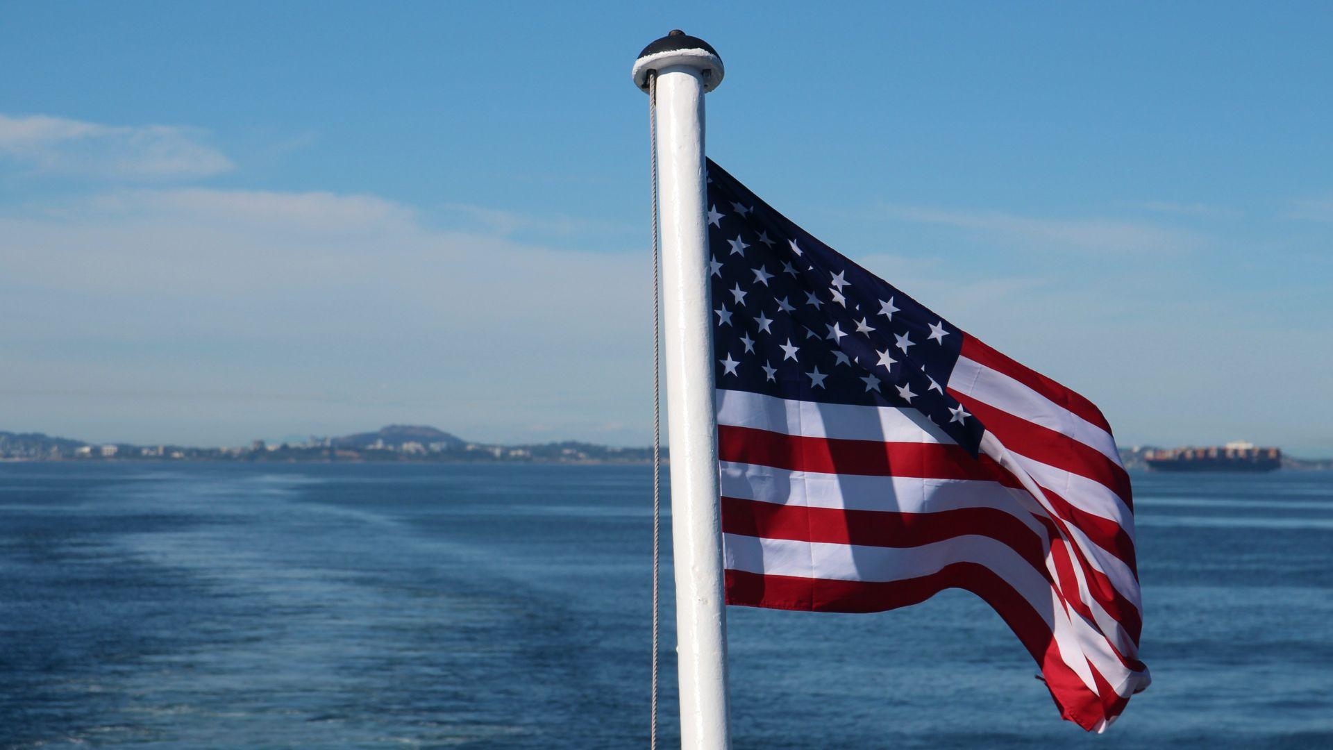An American flag hanging on a pole in front of water.