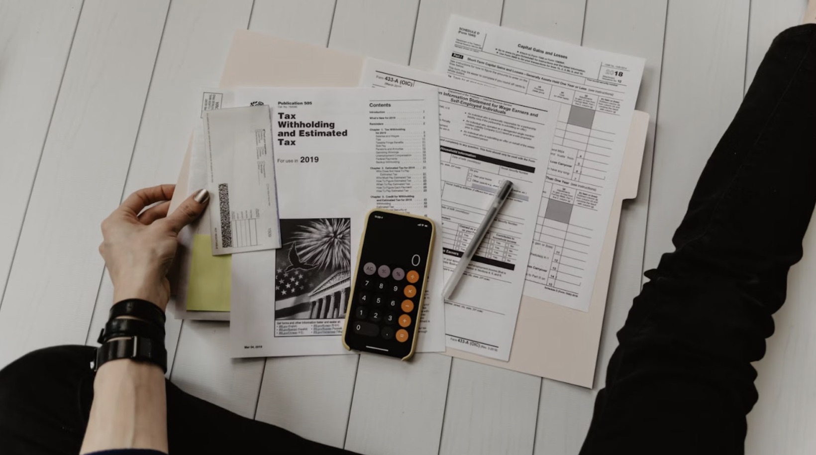 A person sitting on the floor filling out tax forms. A smartphone is on the floor with the calculator app open.