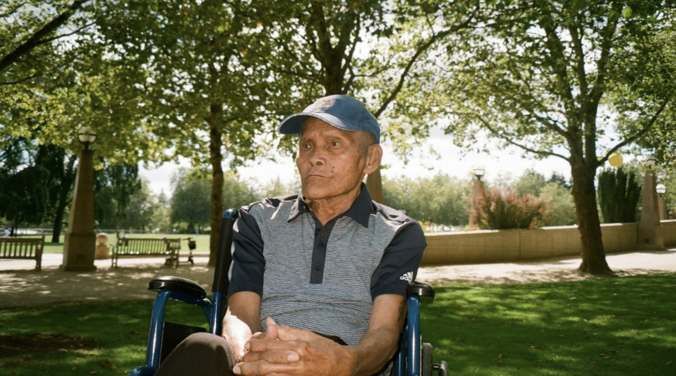 An elderly man in a wheelchair outside at a park.