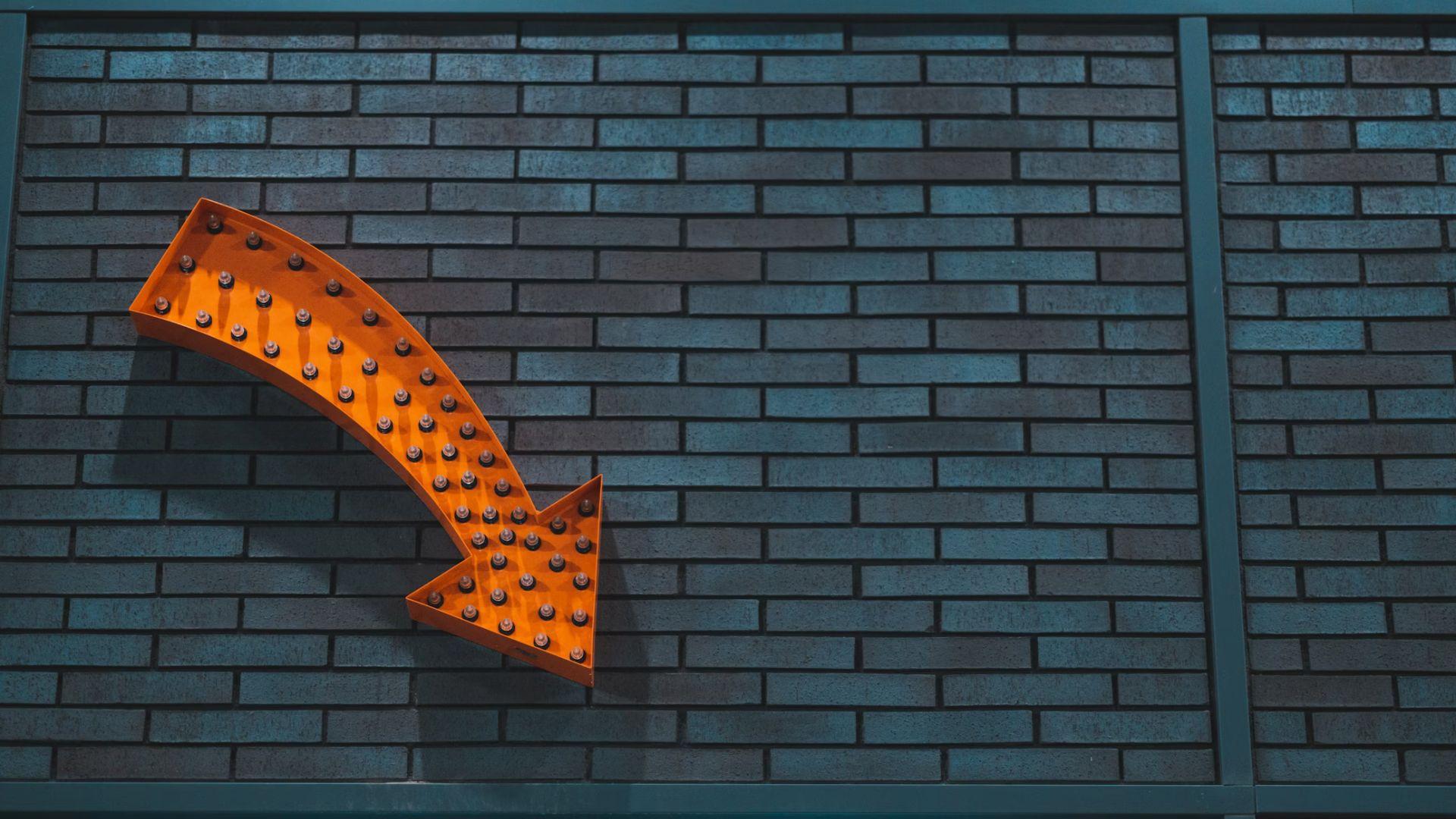 An orange arrow against a brick wall pointing downward.