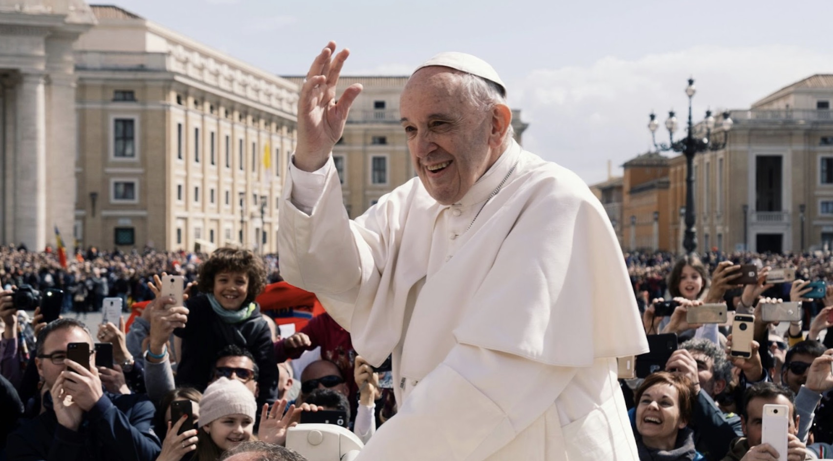 Pope Francis in Vatican City waving to many people.