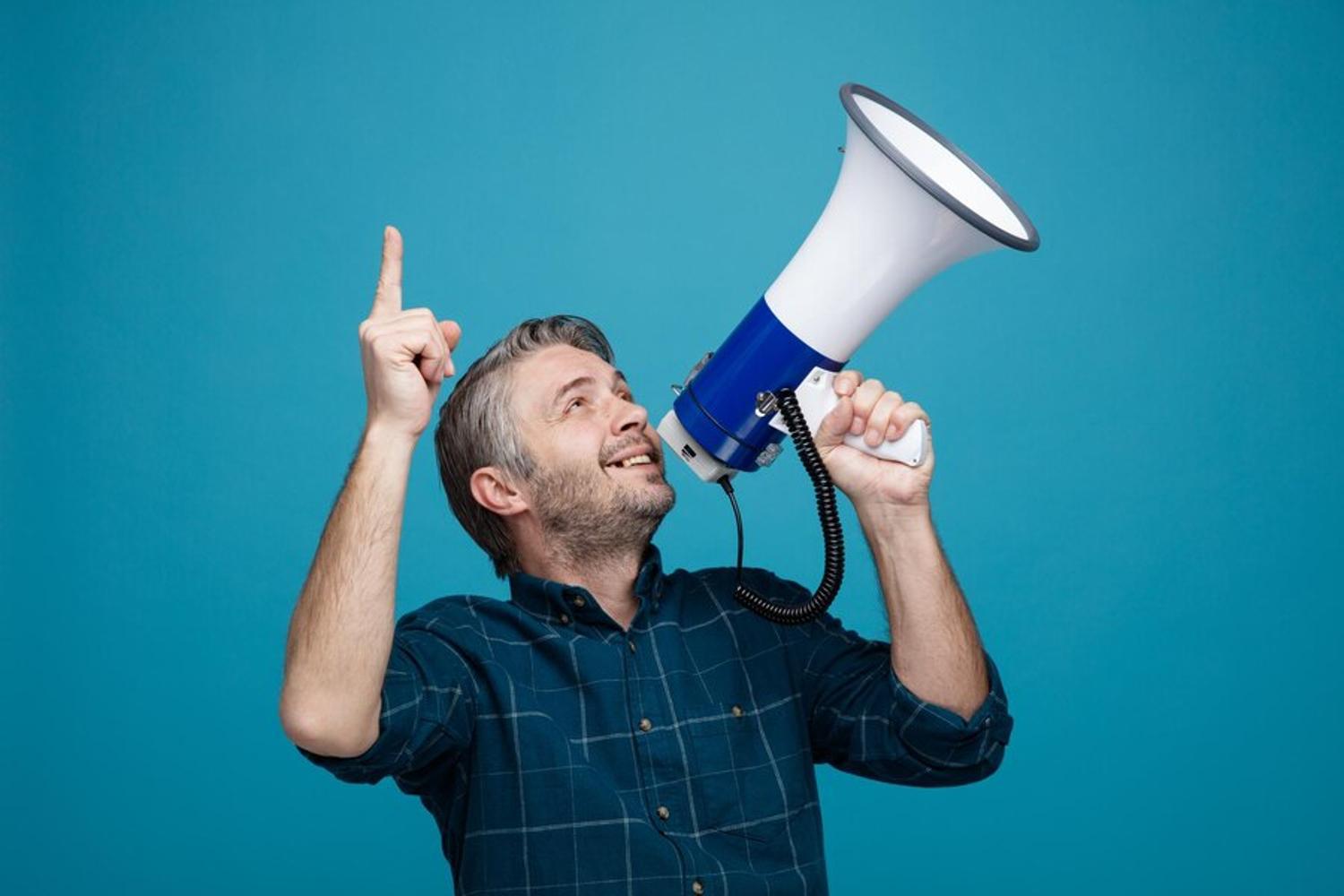 A man smiles as he holds his finger up and speaks into a megaphone