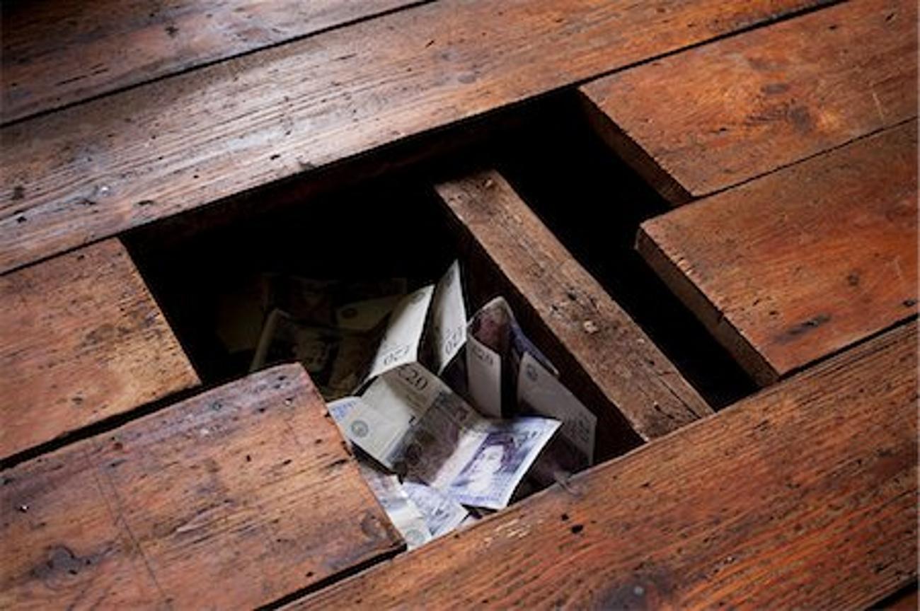 A photograph of a hole in wooden floorboards and the hole is full of British pounds