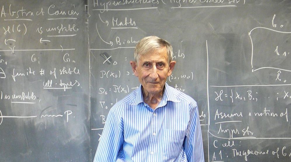 Freeman J. Dyson in a blue button up standing next to a chalkboard
