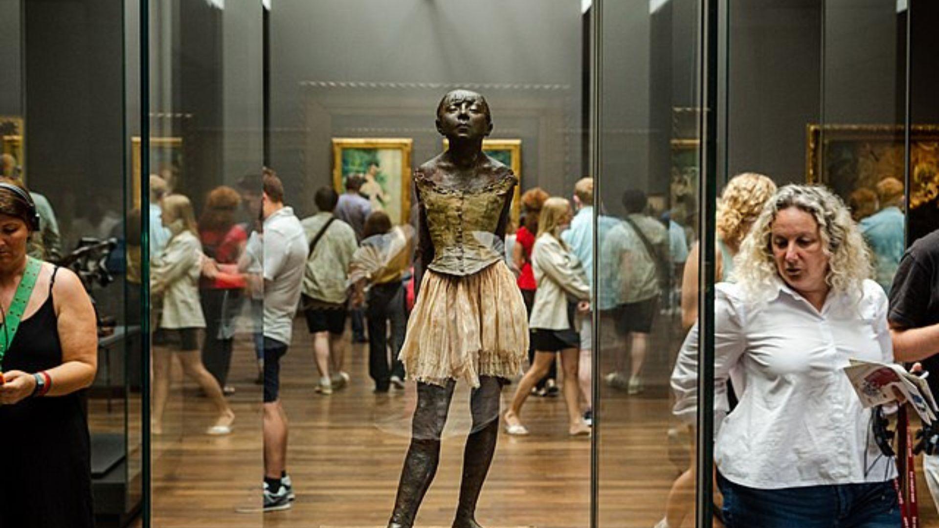 Little Dancer Aged Fourteen statue inside a glass cabinet. People are walking around the statue.
