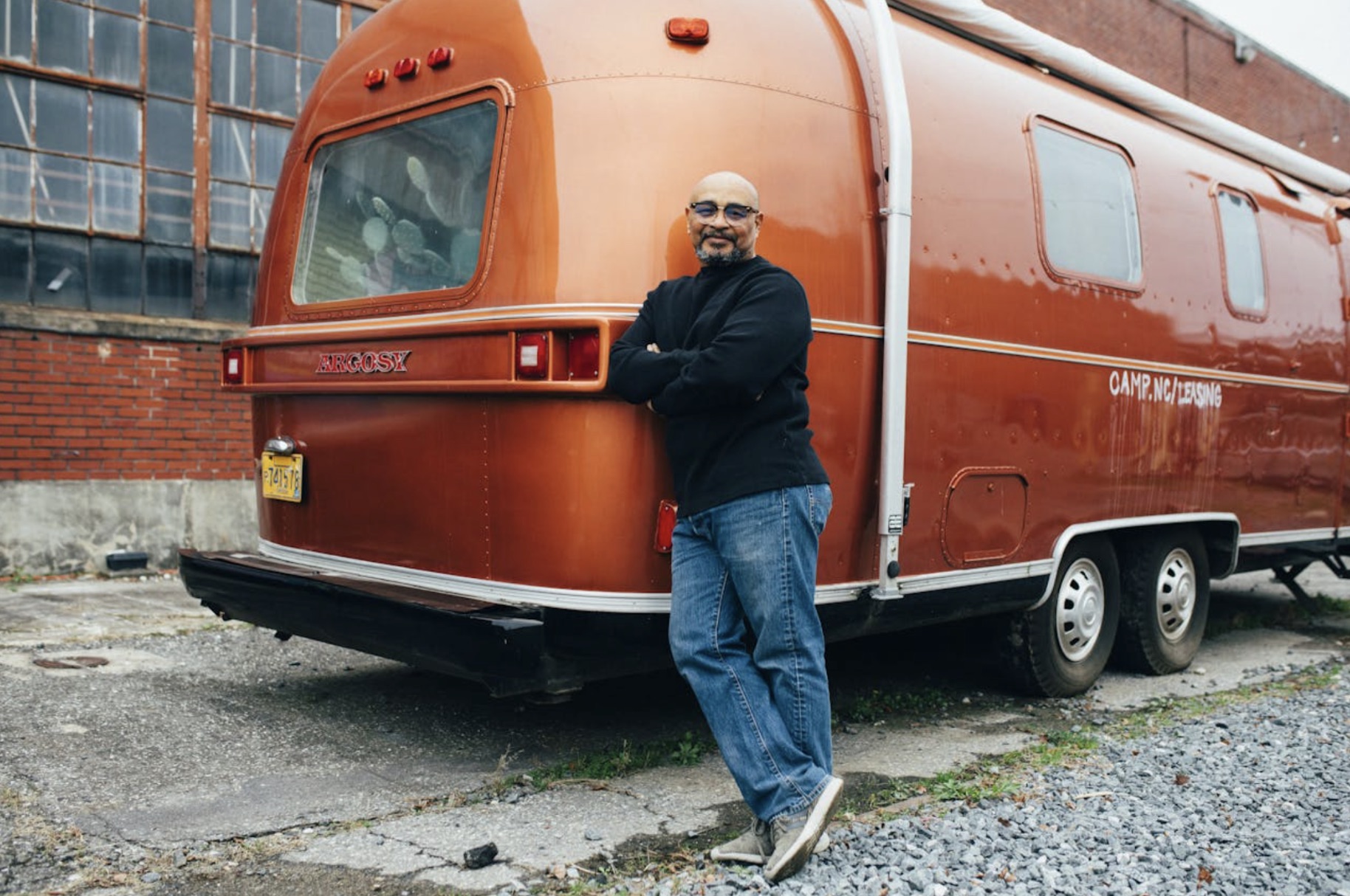 A man is pictured leaning up against his copper-colored RV.