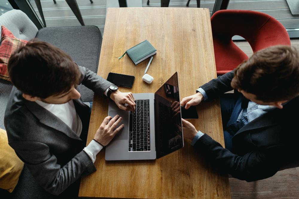 Two men are pictured working at a wooden table