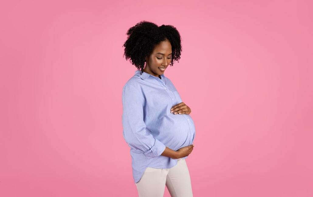 A pregnant black woman dressed in an oversized blue shirt