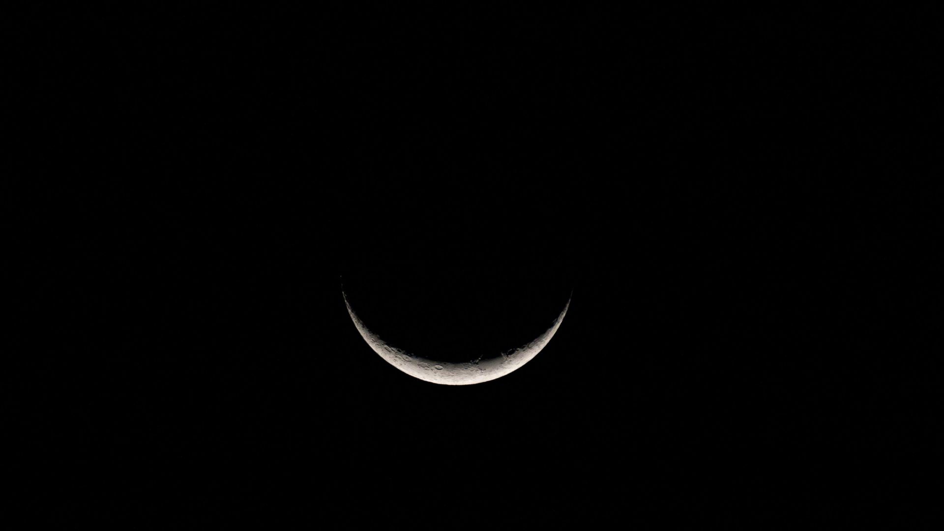 A sliver of a crescent moon seen in the dark night sky.
