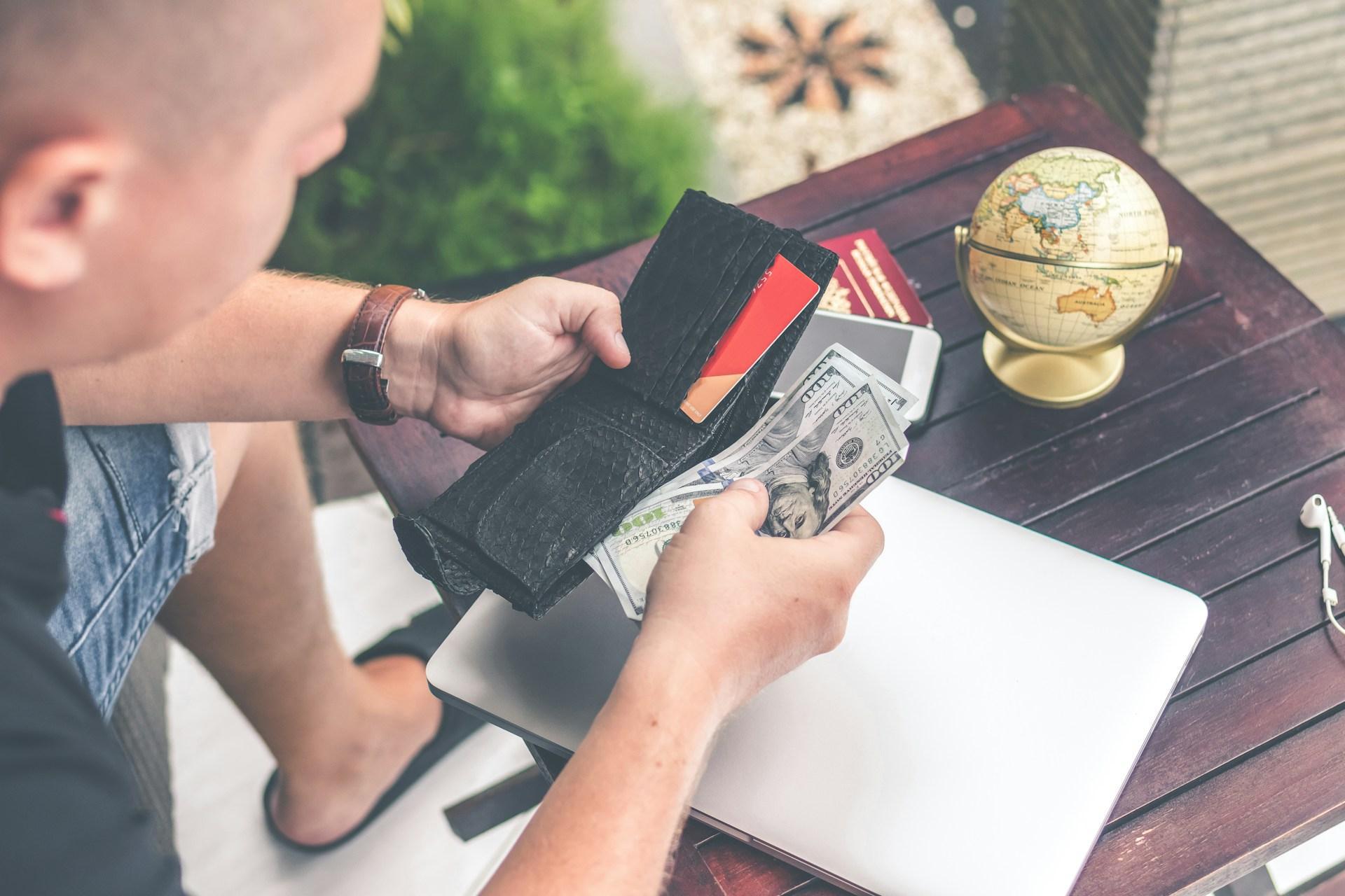 A person holding a wallet and counting the money inside