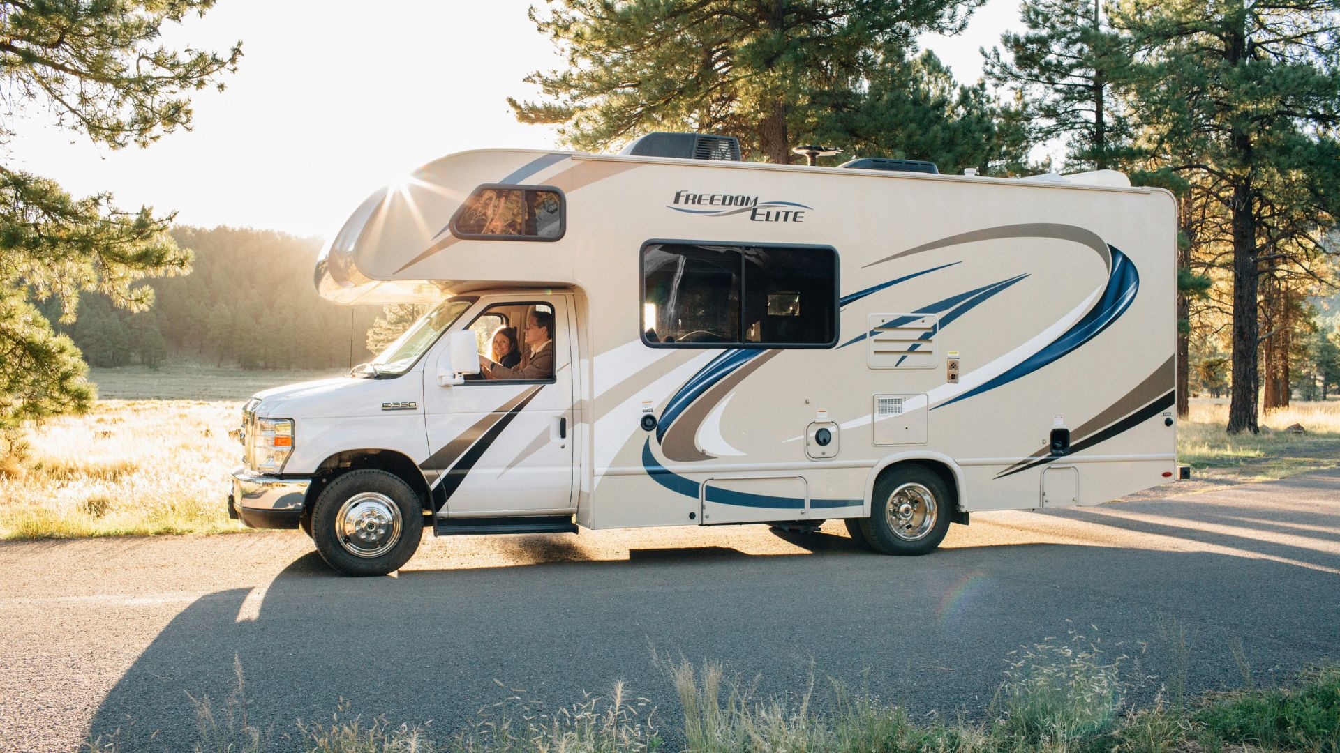A white RV driving down a road with people in it.