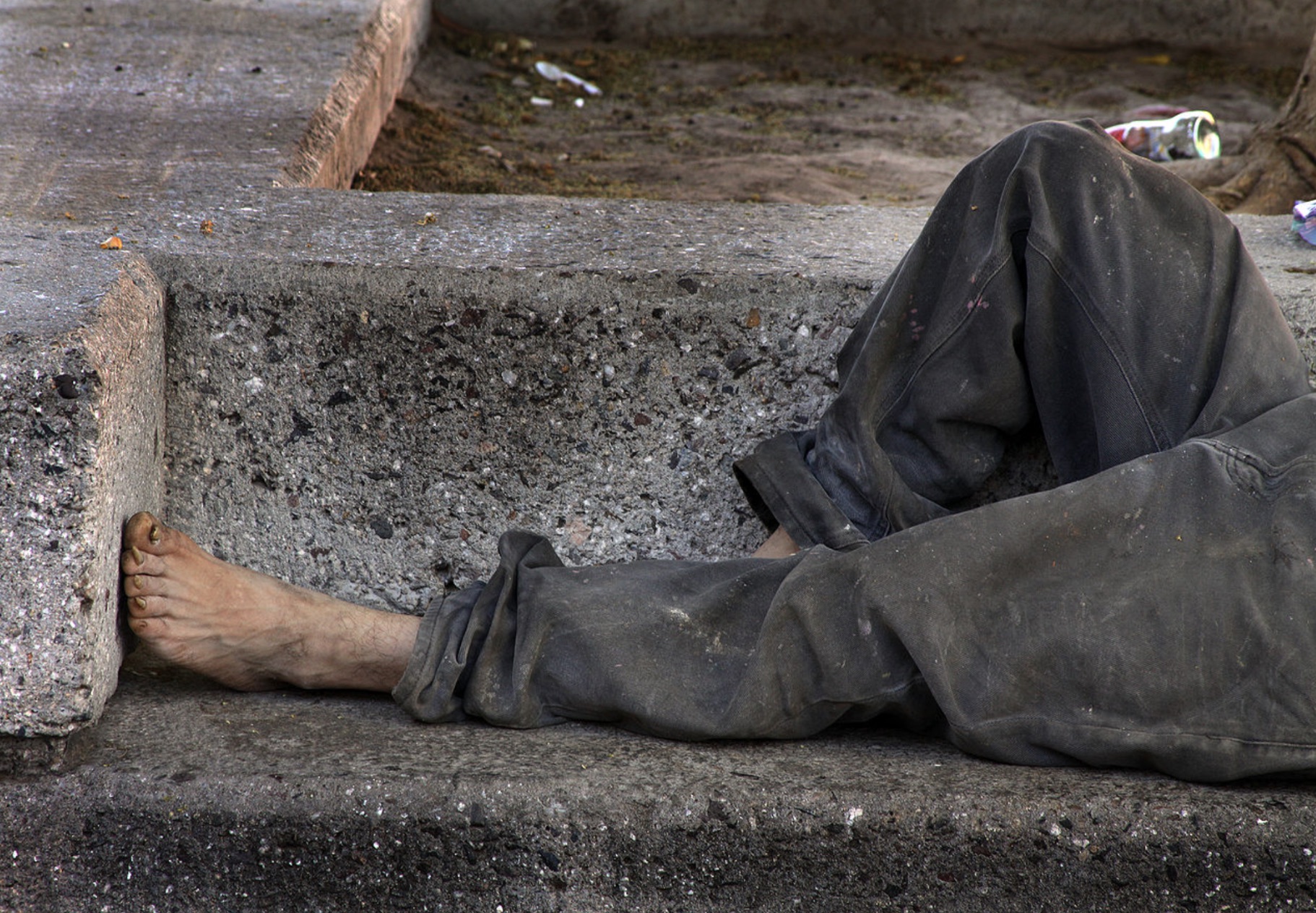 An image of a homeless man resting at the side of a public street