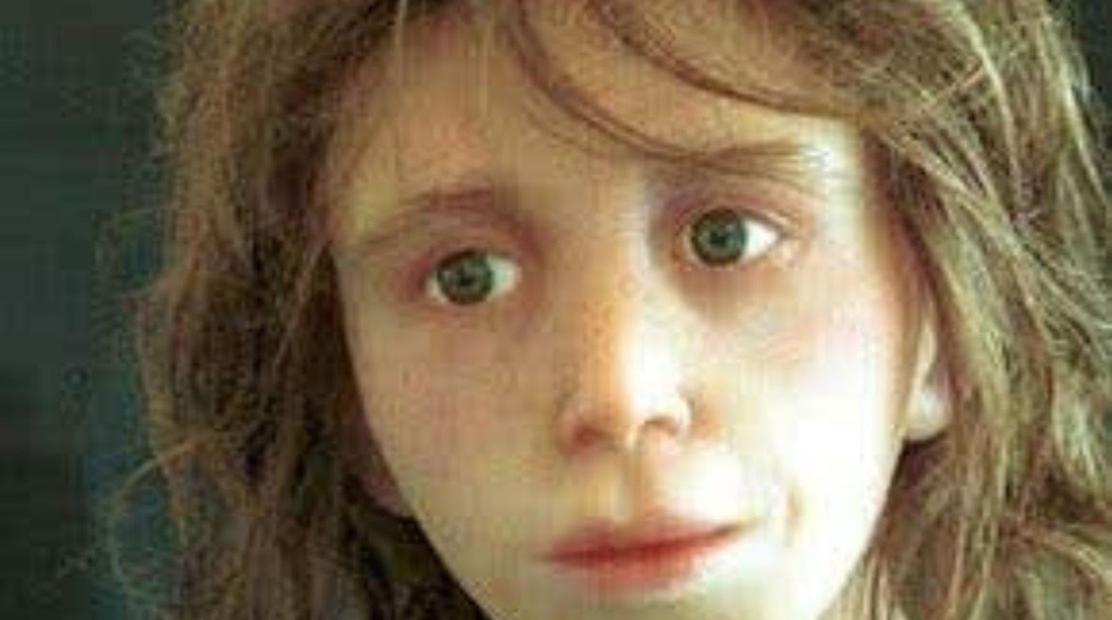 A recreation of what the Lapedo Child would have looked like. He has long brown hair, wide green eyes, a small nose and a mouth protruding slightly outward.