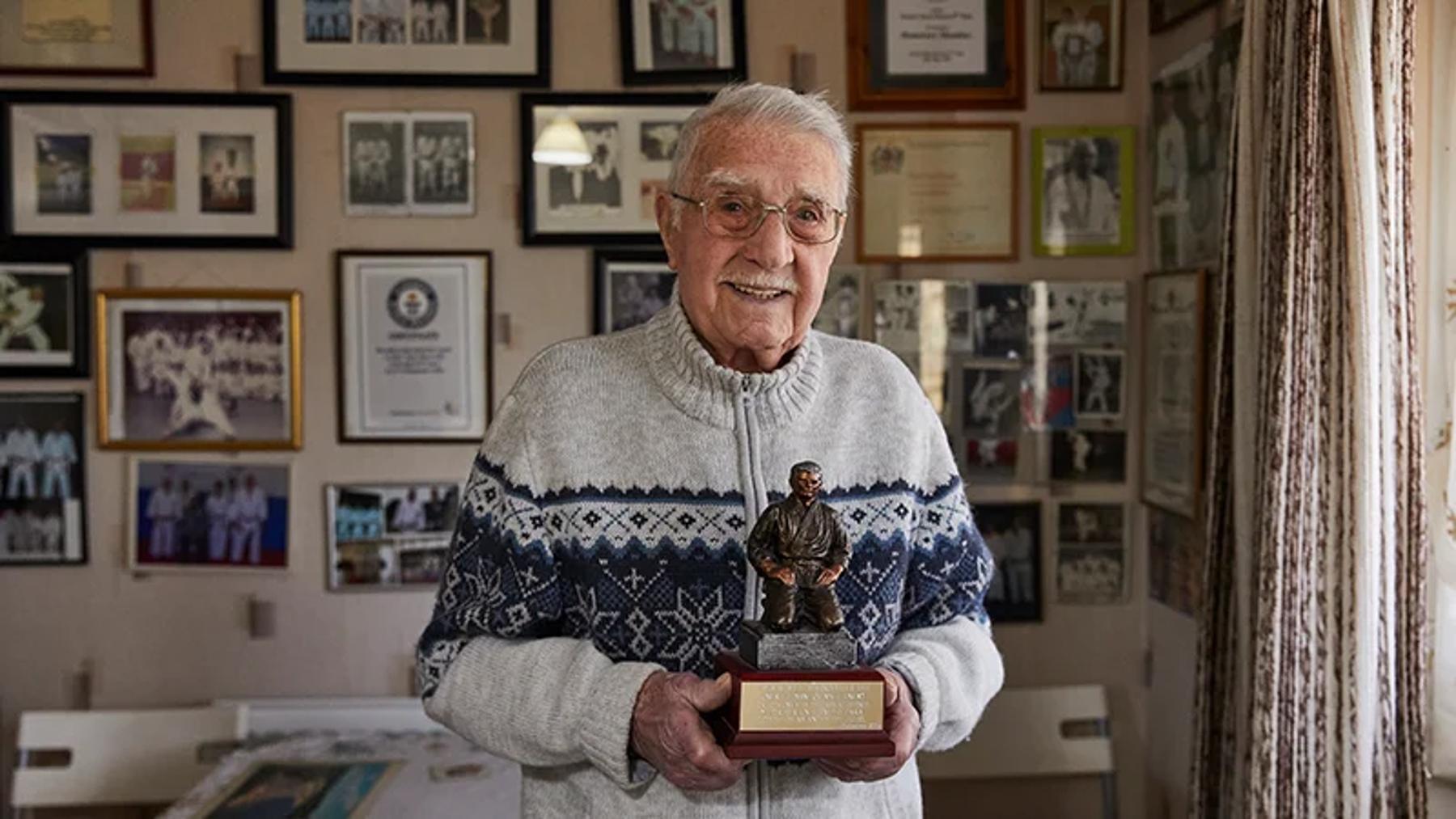 WWII veteran, Jack Hearn, holds an award while standing in his home