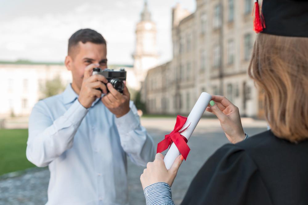 A man in a blue shirt is pictured taking a photograph of a person with their degree