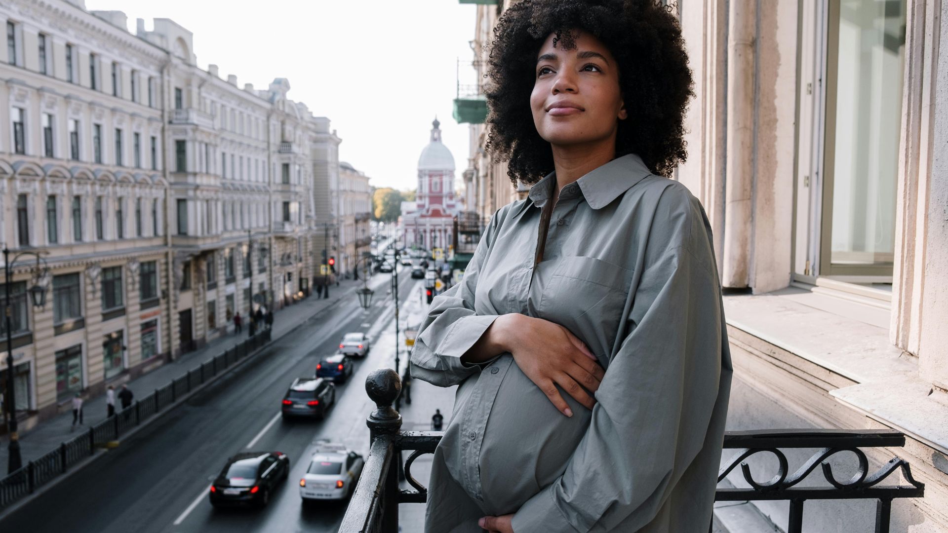 A woman holding her baby bump while standing outside on a balcony in the daytime.
