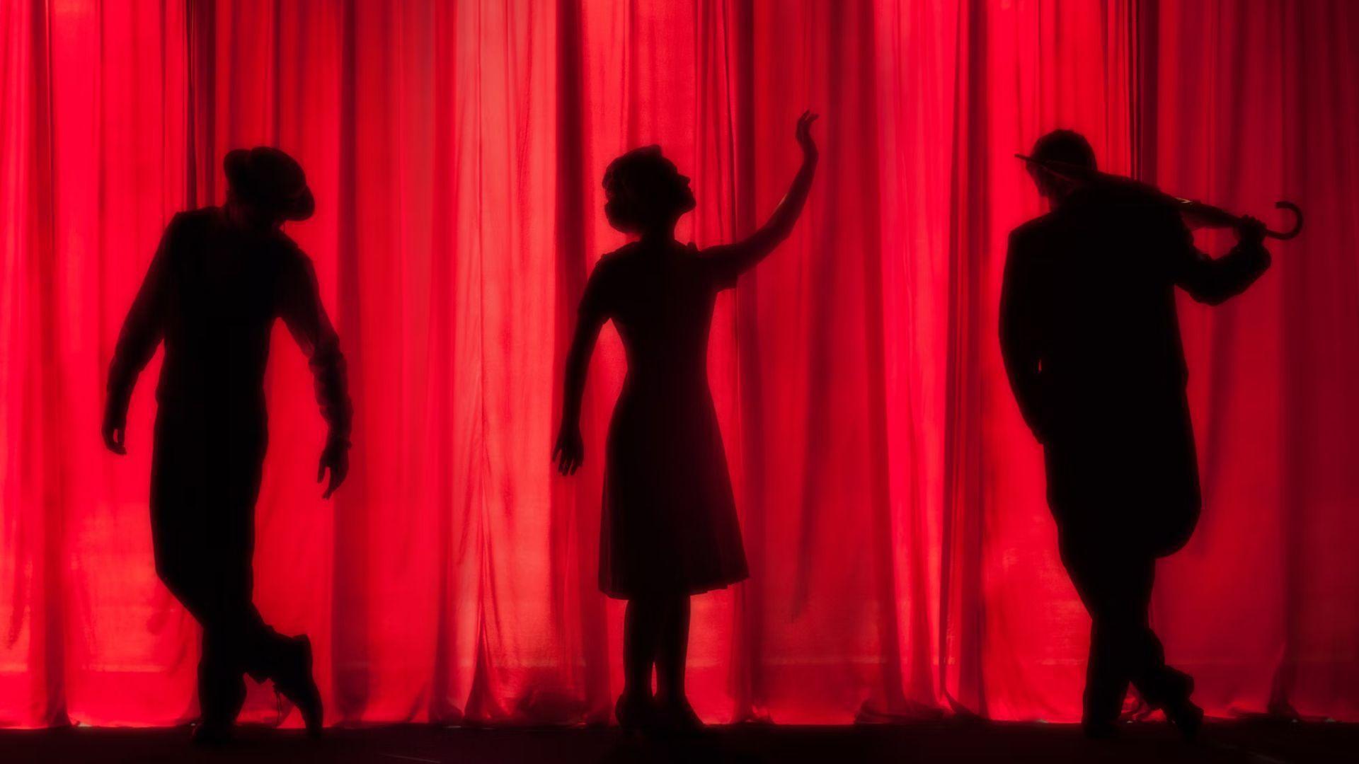 Three black silhouettes behind a red curtain. The one on the left has their legs crossed over, the one in the middle has their arm up and looks out to the side, and the one on the right is holding an umbrella over their shoulders.