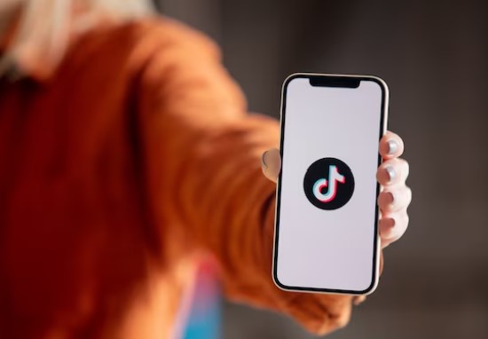 woman in orange top holding up smartphone showing TikTok logo