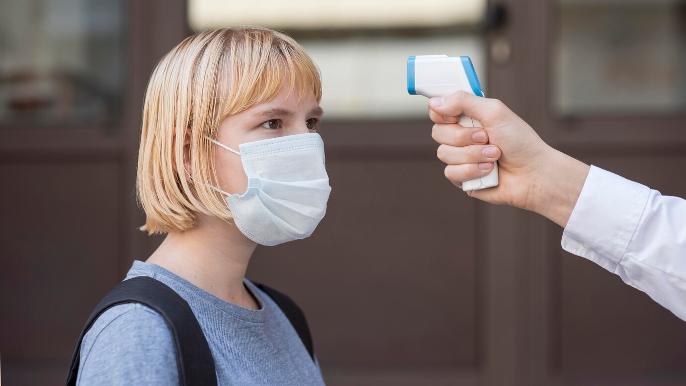 woman wearing face mask getting her temperature checked