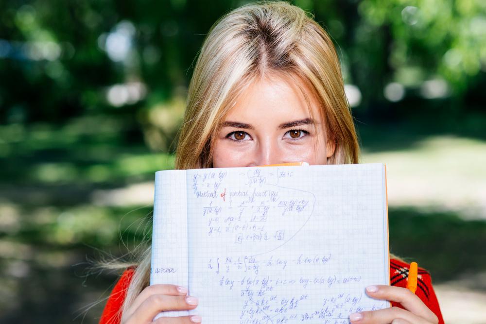 A woman is pictured holding up a small book with several solved equations