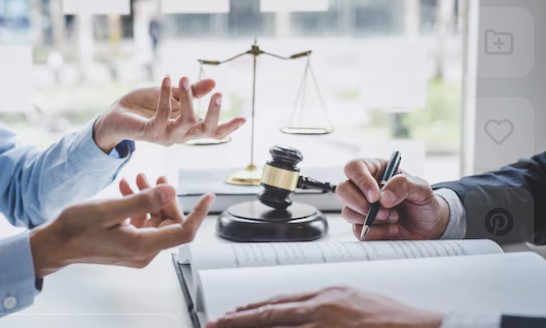 two people sitting at desk having a discussion with person at the right taking notes. There is also a gavel on the desk