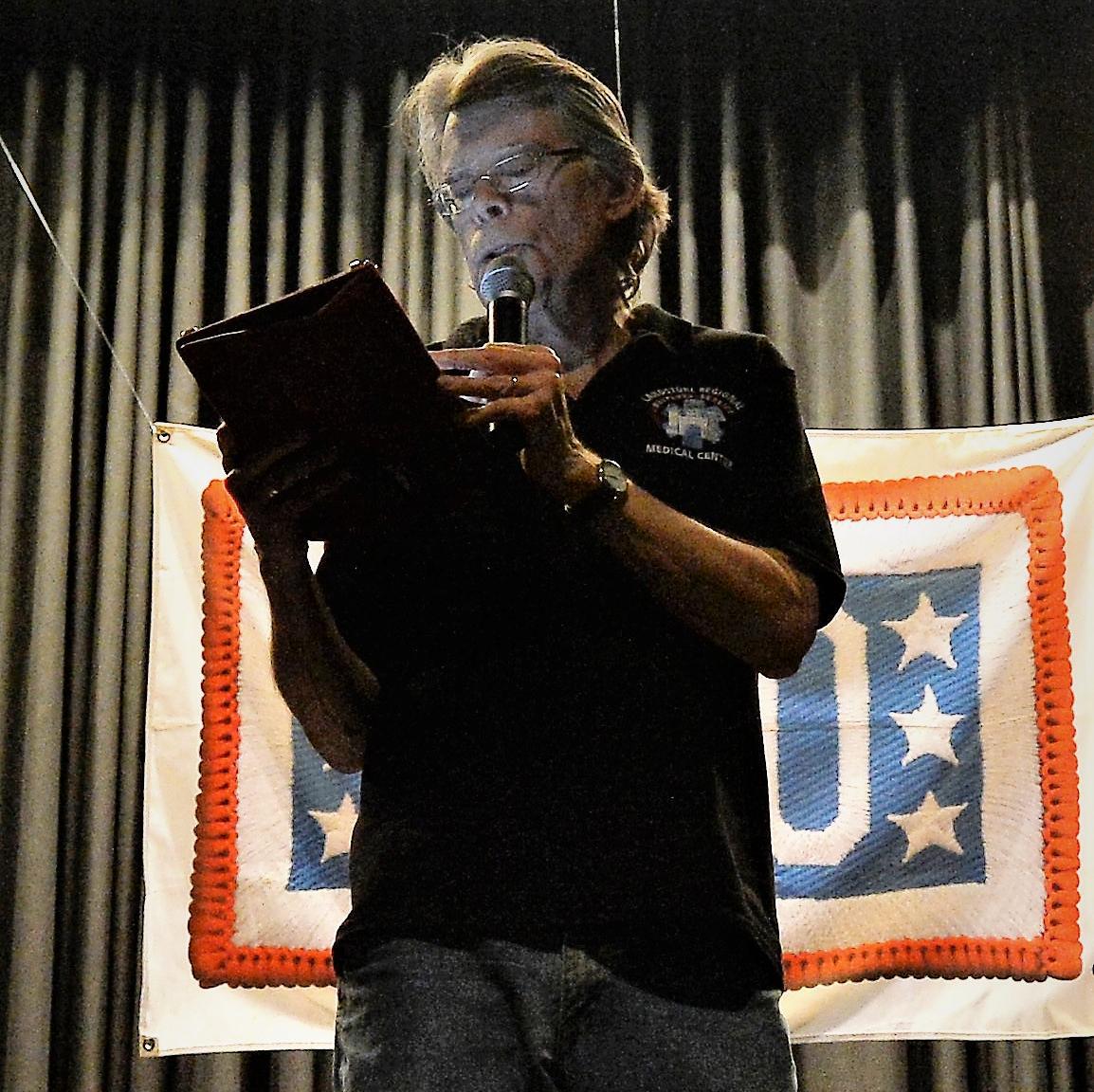 A photograph of Stephen King on stage reading an excerpt from his book