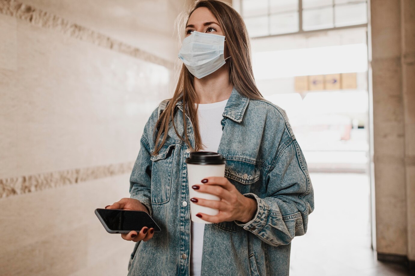 woman walking with coffee and phone in her hands, wearing a face mask