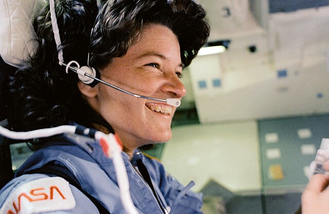 Sally Ride wears a blue astronaut uniform with a head peace