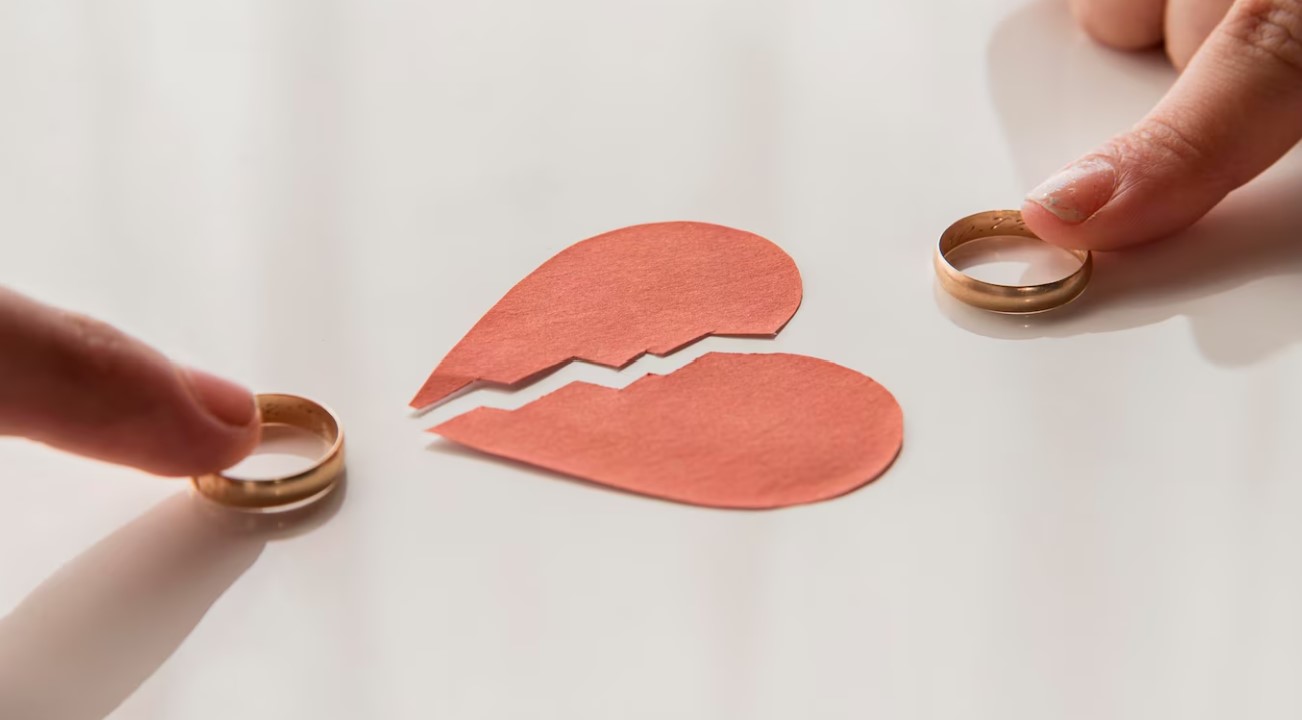Paper broken-heart with two index fingers holding down a ring on each side